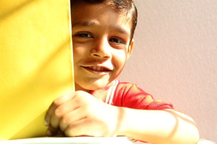 little boy smiling and peaking out from behind book