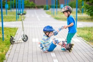 young boy helping his friend on roller skates stand up - by Pahis / istock