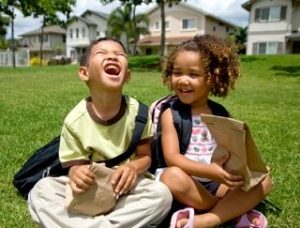 cheerful preschooler boy and girl sitting together on grass with bag lunches