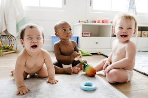 three babies on floor, two sitting up, one crawling