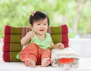 infant girl sitting on the floor with her back and side propped up against cushions