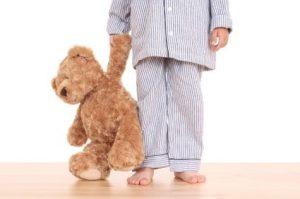 preschool aged child photographed from chest down, in pajamas holding teddy bear
