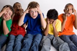 5 young boys sitting together on a bench, each holding their faces and making angry or disturbed facial expressions