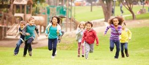 seven school age children, diverse ethnicities, running happily on the grass at a park