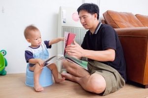 father sitting with and reading to young child on potty chair