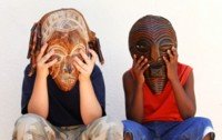 two children seated together, each wearing wooden abstract masks