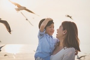 mother and child laughing on beach together, seagulls