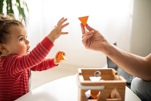infant reaching for shape toy held by mother