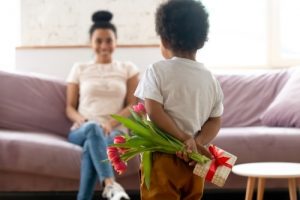 toddler, viewed from behind, concealing a gift of flowers for mother